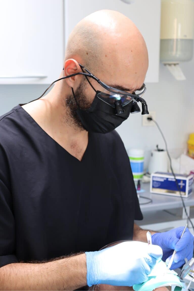 Dentista de la clínica con gafas de aumento tratando a un paciente en el gabinete