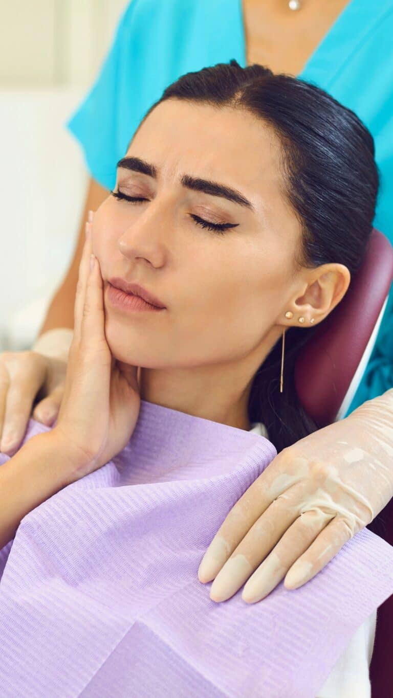 Paciente con dolor de muelas en el sillón dental, con la mano en la mejilla